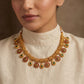 Woman wearing a gold necklace with floral designs on a beige background