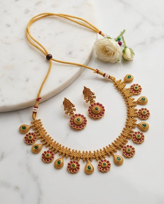 Gold necklace and earrings set on a marble surface with flowers.