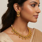 Woman wearing gold jewelry with green gemstones on a neutral background